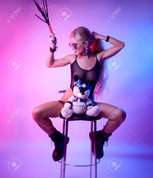 155490885-sexy-blonde-with-long-hair-sits-on-a-chair-with-a-toy-bear-in-bdsm-accessories